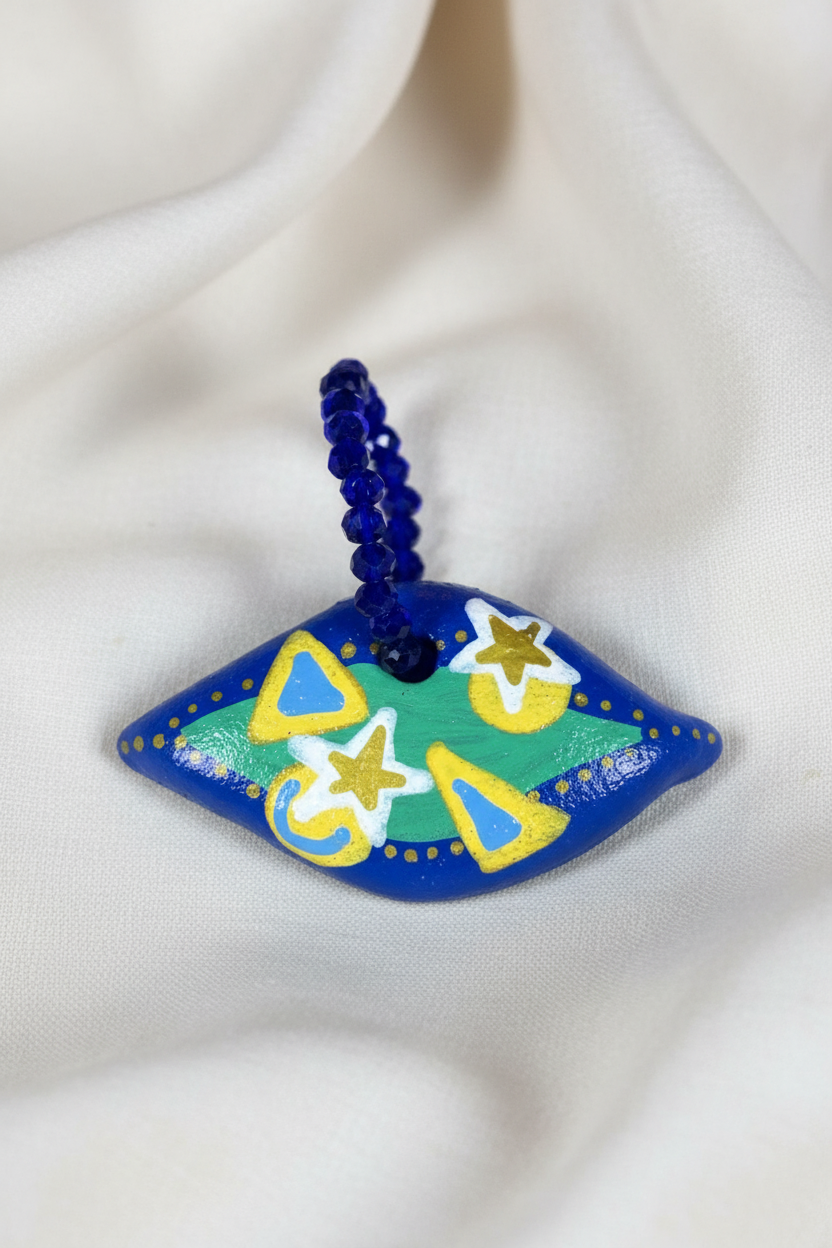 Pingente azul losango com círculo verde em close sobre tecido fluido