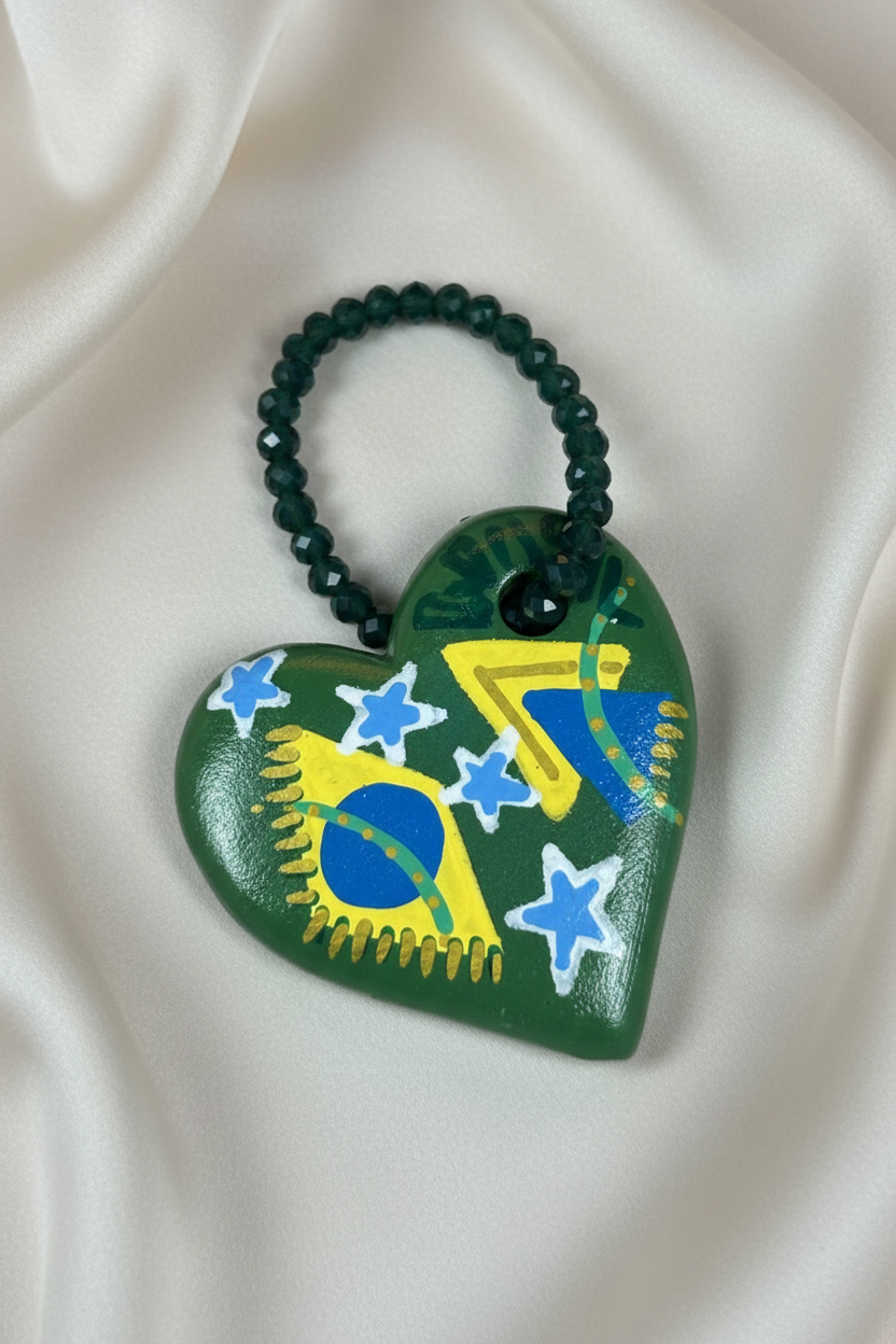 Pingente em formato de coração verde com bandeira do Brasil em close sobre tecido fluido